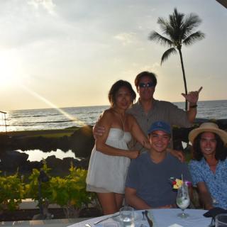 A group of people enjoying a sunset dinner by the beach.