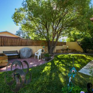 A sunny backyard garden with lush grass, a large tree providing shade, and a cozy outdoor seating area.