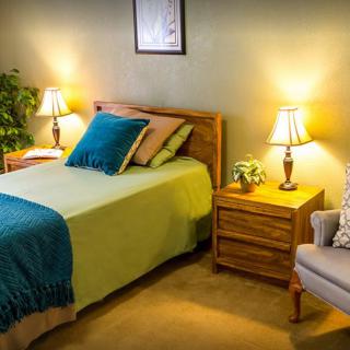 A cozy bedroom featuring a bed with colorful pillows, two bedside lamps, and a comfortable chair.