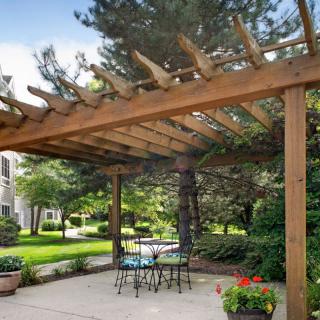 A cozy backyard patio with a wooden pergola and outdoor seating surrounded by lush greenery.