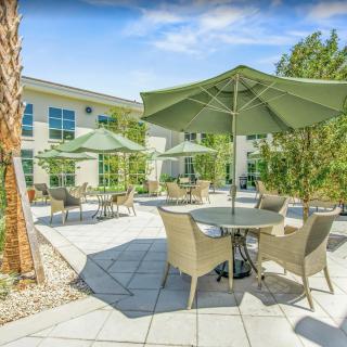 A sunny outdoor patio area with tables, chairs, and large umbrellas.