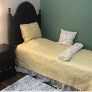A neatly made single bed with yellow bedding and pillows, accompanied by a wooden nightstand.