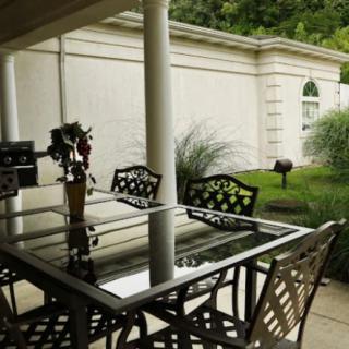 Outdoor patio area with a glass table and decorative chairs overlooking a garden.