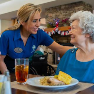 A caregiver smiling and interacting with a senior woman during mealtime.