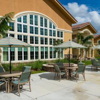 A sunny patio area with tables and umbrellas in front of a building featuring large arched windows.