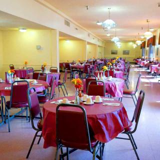 An empty dining room with tables and chairs neatly arranged, covered with red tablecloths.