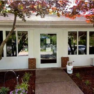 A house entrance with a glass door, surrounded by windows and landscaped greenery.