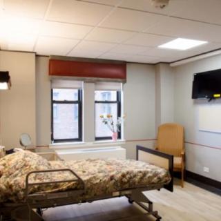 A hospital room featuring a patient bed, chair, and television.
