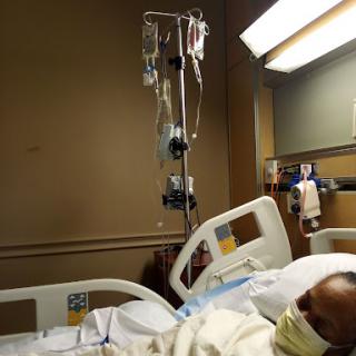 A patient resting in a hospital bed with an IV drip overhead.