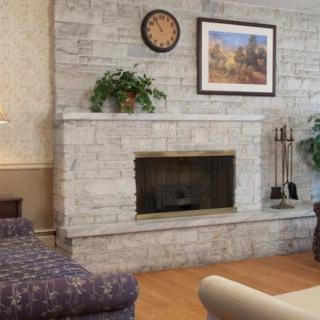 A cozy living room featuring a stone fireplace, decorated with a painting and a clock.