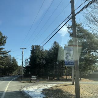 A scenic view of a road lined with trees and power lines under a clear blue sky.
