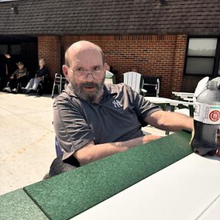 A man enjoying a sunny day outdoors, seated at a table.
