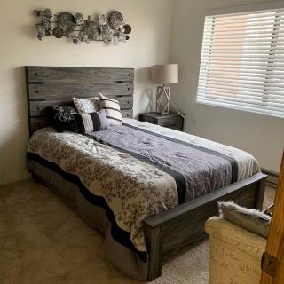 A cozy bedroom with a large bed, decorated with pillows and a modern wall art piece. A lamp is placed on a bedside table near the window.