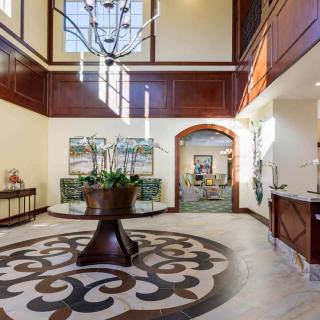 A spacious and elegant lobby featuring a chandelier, wood paneling, decorative flooring, and a central plant display.