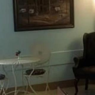 A cozy room with a small round table, two chairs, an armchair, and a wall painting under soft lighting.