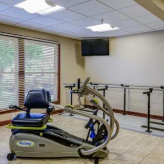 A rehabilitation room featuring exercise equipment, including a recumbent bike and parallel bars.