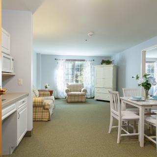 A cozy living space with a dining area and kitchen, featuring natural light and comfortable furniture.