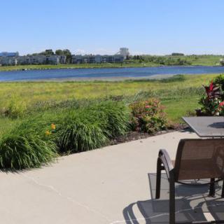 A serene patio with a beautiful lake view, surrounded by lush greenery and gardens.