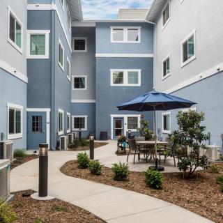 A modern apartment building featuring a courtyard with outdoor seating and a patio umbrella.