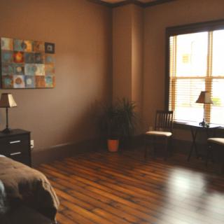 A cozy bedroom with hardwood flooring, modern decor, and natural light streaming through the window.