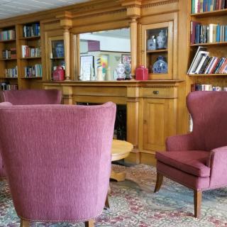 A cozy library corner with armchairs and wooden shelves filled with books.