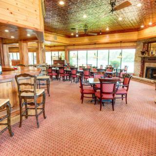 A cozy restaurant dining area with wooden interiors, featuring tables and chairs, a bar area, and large windows offering natural light.