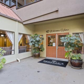 An inviting entrance to a building with large glass doors, adorned with potted plants and a welcome mat.