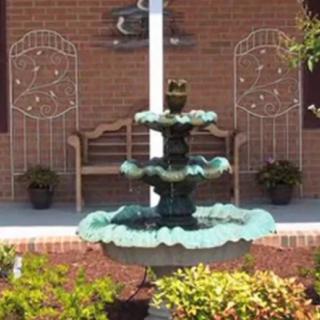A decorative fountain in front of a brick wall, flanked by a bench and potted plants.