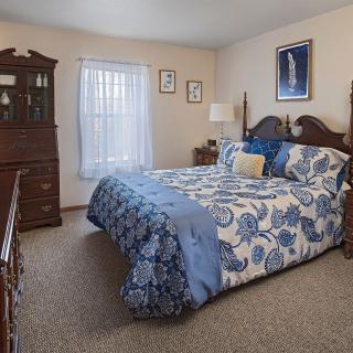 A cozy bedroom with a blue and white floral bedspread, wooden furniture, and soft lighting.
