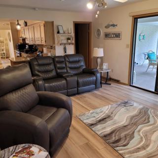 A cozy living room with leather recliners, a patterned rug, and an open view into the kitchen through a wide sliding glass door.