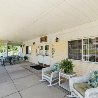 A covered patio with outdoor seating, featuring chairs, tables, and decorative plants.