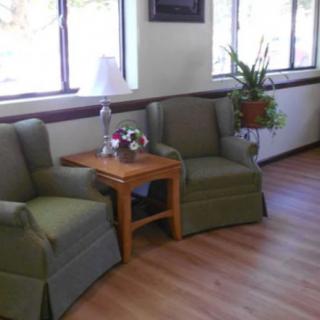 A cozy seating area with two green chairs and a wooden table, adorned with plants and decorative items.