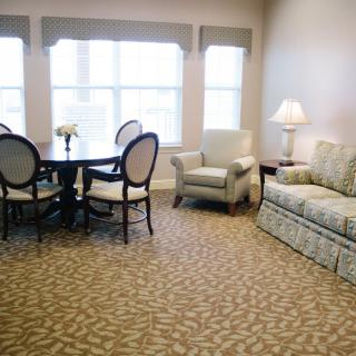 A cozy living room with a sofa, armchair, and a dining table near large windows.