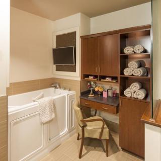 A cozy bathroom featuring a walk-in bathtub and wooden shelving stocked with neatly rolled towels.
