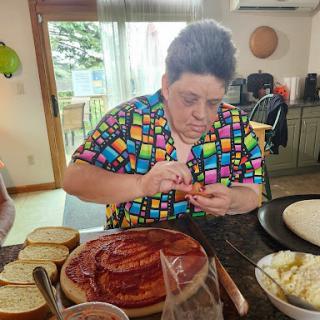 A person in a colorful shirt carefully assembles ingredients for pizza in a cozy kitchen.