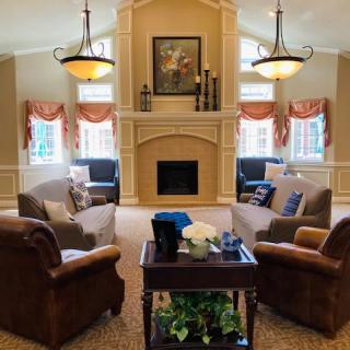 A cozy living room with comfortable seating, a central fireplace, and elegant chandeliers.