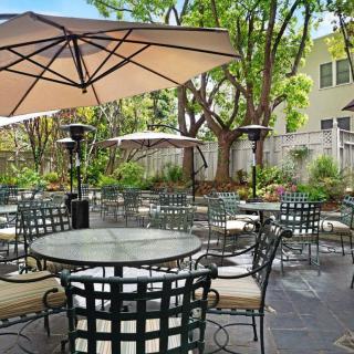 A serene outdoor patio area with tables, chairs, and umbrellas surrounded by greenery.