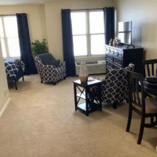 A cozy living room with patterned furniture, a carpeted floor, and large windows.
