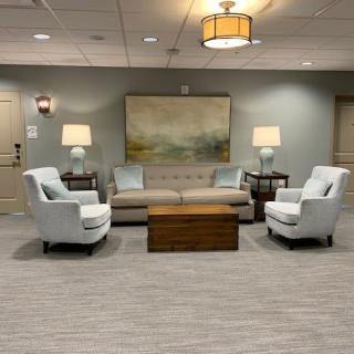 A cozy seating area with a sofa, two armchairs, and a coffee table, accented by lamps and artwork.