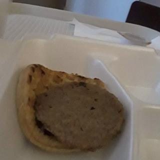 A burger patty on a bun inside a takeout container.