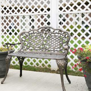 A decorative metal bench surrounded by flower pots against a lattice backdrop.