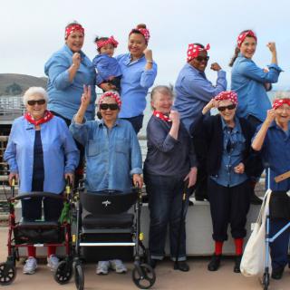 A group of women wearing matching costumes and bandanas pose and smile outdoors.