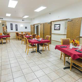 An indoor dining room with tables covered in red tablecloths and chairs arranged around them.