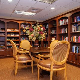 A cozy library room with wooden bookshelves, a table, and chairs arranged around it, featuring a decorative flower arrangement.