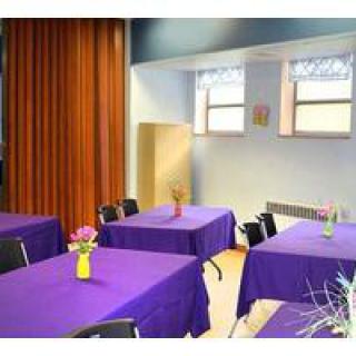 A decorated event space with tables covered in purple tablecloths, each adorned with vases of flowers.