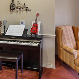 A cozy music room featuring a piano with sheet music and a red ukulele, complemented by a comfortable armchair.