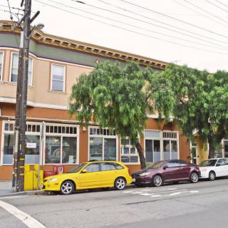 A street view of a two-story building with cars parked in front and trees lining the sidewalk.