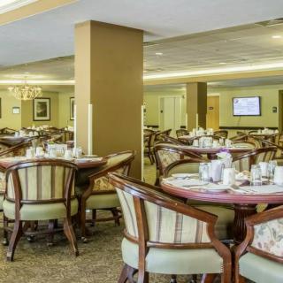 A spacious dining area with elegantly arranged tables and chairs, featuring soft lighting and a carpeted floor.