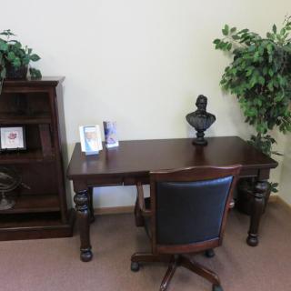 A classic office setup with a wooden desk, chair, bookshelf, and decorative plants.