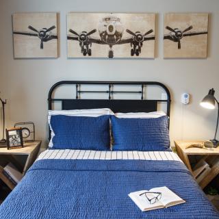 A stylish bedroom with aviation-themed artwork above the bed, featuring industrial elements and blue bedding.
